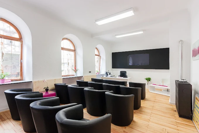 Unterrichtsraum in Lohr: Sessel in Reihen vor einer Tafel mit Bildschirm, Bogenfenster an der Seite.